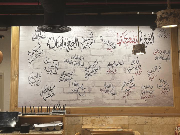 Restaurant wall covered with hand-lettered Arabic phrases in black and red on a whitewashed brick texture