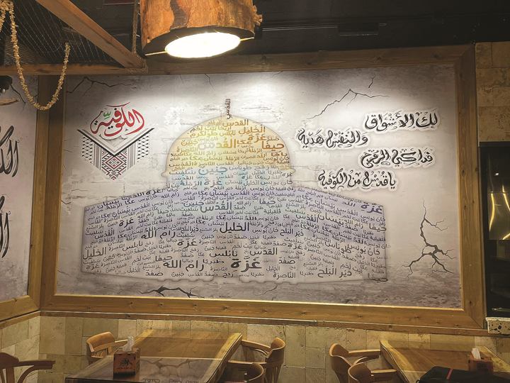 Restaurant wall with the Dome of the Rock drawn from hand-lettered Arabic words, framed in wood above stone cladding