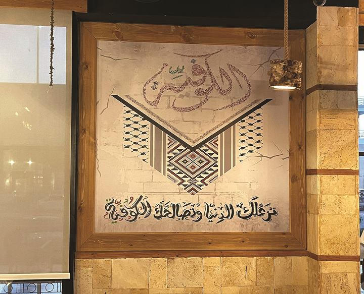 AlKofeia emblem painted on a wall with a keffiyeh pattern and Arabic calligraphy, framed in wood