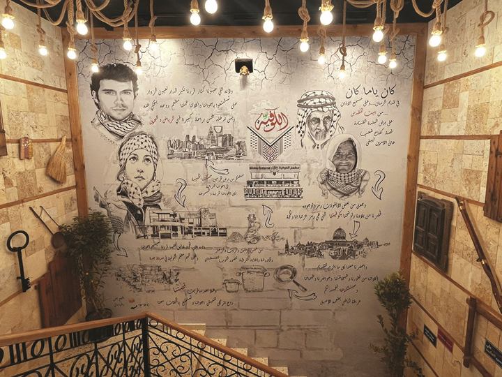 Stairwell wall mural at AlKofeia with hand-drawn portraits, landmarks and Arabic handwriting under hanging bulbs
