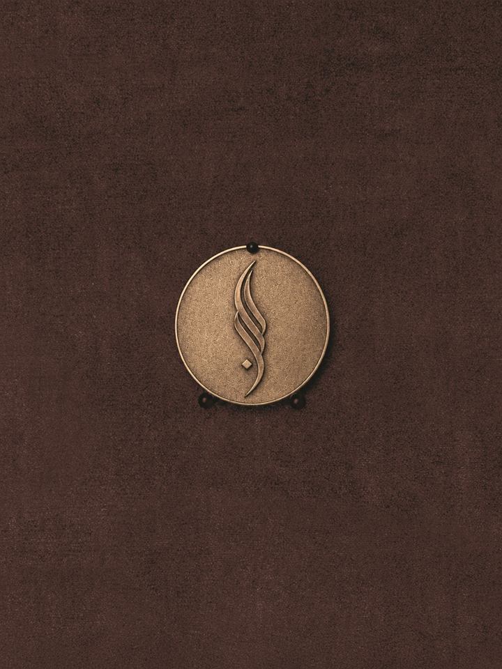 Round bronze medallion bearing the SALLY NAJJAR calligraphic emblem, mounted on a dark cocoa textured wall